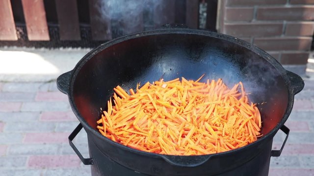 Uzbek national dish pilaf in a large cast-iron cauldron on the fire, add sliced red carrots, rice, lamb, mutton fat, the fat tail, sesame oil, onion, garlic, red hot chili pepper