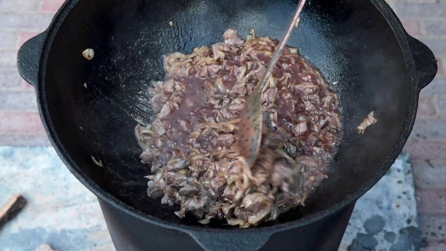 Uzbek national dish pilaf in a large cast-iron cauldron on the fire, add sliced red carrots, rice, lamb, mutton fat, the fat tail, sesame oil, onion, garlic, red hot chili pepper