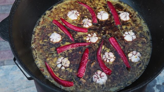 Uzbek national dish pilaf in a large cast-iron cauldron on the fire, sliced red carrots, cold water, add whole of garlic and red chili peppers, rice, lamb, mutton fat, the fat tail, sesame oil, onion
