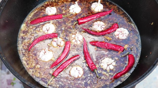 Uzbek national dish pilaf in a large cast-iron cauldron on the fire, sliced red carrots, cold water, add whole of garlic and red chili peppers, rice, lamb, mutton fat, the fat tail, sesame oil, onion
