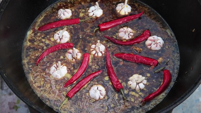Uzbek national dish pilaf in a large cast-iron cauldron on the fire, sliced red carrots, cold water, add whole of garlic and red chili peppers, rice, lamb, mutton fat, the fat tail, sesame oil, onion