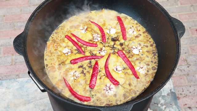 Uzbek national dish pilaf in a large cast-iron cauldron on the fire, sliced red carrots, cold water, add whole of garlic and red chili peppers, begins to boil, rice, lamb, mutton fat, the fat tail