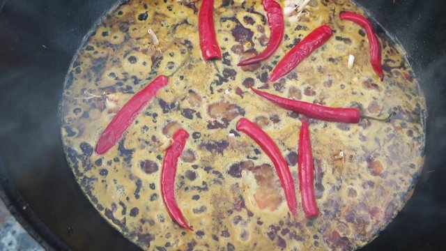 Uzbek national dish pilaf in a large cast-iron cauldron on the fire, sliced red carrots, cold water, add whole of garlic and red chili pepper, boiling, rice, lamb, mutton fat, the fat tail, sesame oil