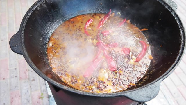 Uzbek national dish pilaf in a large cast-iron cauldron on the fire, sliced red carrots, added barberry, garlic is removed and red chili pepper, boiling, rice, lamb, mutton fat,  fat tail, sesame oil