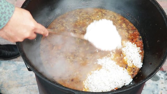 Uzbek national dish pilaf in a large cast-iron cauldron on the fire, sliced red carrots, added barberry, garlic is removed and red chili pepper, added rice, lamb, mutton fat, the fat tail, sesame oil