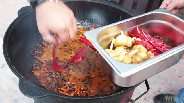 Uzbek national dish pilaf in a large cast-iron cauldron on the fire, sliced red carrots, added barberry, garlic is removed and red chili pepper, added rice, lamb, mutton fat, the fat tail, sesame oil