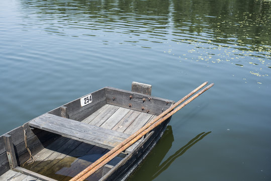 Fragment Of Traditional Wooden Fishing Boat With Oars Attached In Still Water Of River