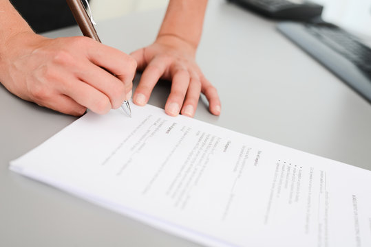 close-up shot of hands signing a contract on desk in office