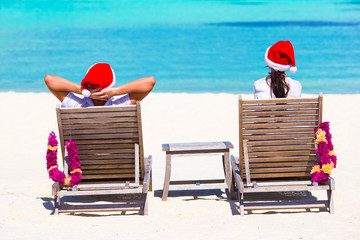 Young couple in Santa hats relaxing on beach during Christmas