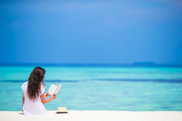 Young woman reading on tropical white beach