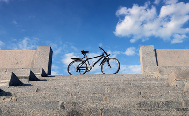 Bike stands on the stone steps on the background of blue sky