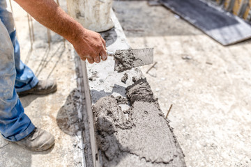 Construction industry worker using a putty knife and leveling concrete on concrete pillars