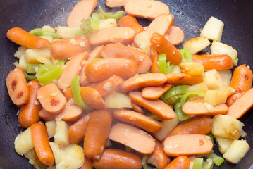 Preparing a stir fry of stewed vegetables and sausage