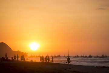 Fototapeta na wymiar People walking on the beach of Mancora during orange sunset