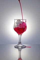 Pouring red syrup on ice with gray background.