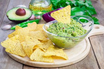Bowl with chunky guacamole served with nachos and ingredients on backgroung