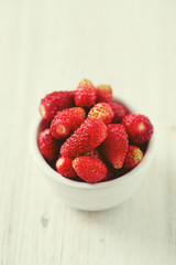 wild strawberries in a bowl on wooden surface