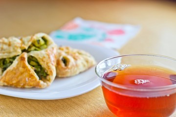 Fresh baked homemade puff pastry cakes with fresh strong black tea in glass cup. Close up