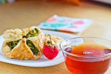 Fresh baked homemade puff pastry cakes, strawberry with fresh strong black tea in glass cup. Selective focus