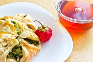 Fresh baked homemade puff pastry cakes, strawberry with fresh strong black tea in glass cup