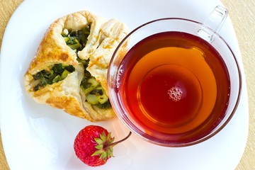 Fresh baked homemade puff pastry cakes, strawberry with fresh strong black tea in glass cup. Top view