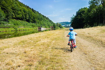 young boy with helmet riding bike off the road near river