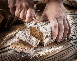 Man's hands cutting bread on the wooden plank.