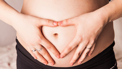 Pregnant Woman holding hands in a heart shape on her baby bump. 