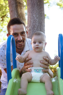 Bebe en brazos de su padre jugando en el parque. Primer plano de un padre jugando con su bebe desnudo en pañal. Bebe feliz.