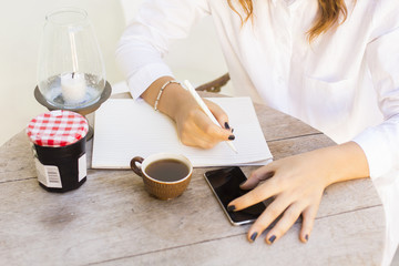 girl at the table writing in a notebook with a cell phone and te