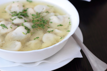 Bowl of broth with small meat dumplings and chives.