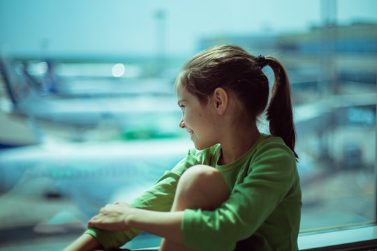 Child at the airport near the window looking at airplanes and waiting for time of flight.