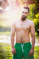 Sports man with brown hair and a beard on a background of green meadows