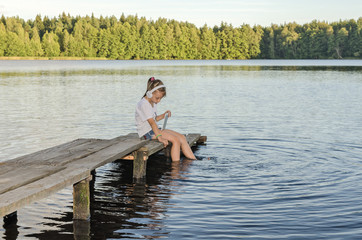Fototapeta na wymiar ГАРМОНИЯ/ Девочка слушает музыку сидя на деревянном мостике на озере. 