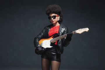 Fototapeta premium Rocker Girl Holding a Guitar Against Black Wall