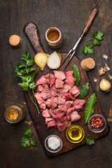 Raw meat for Goulash preparation with oil and fresh herbs and spices on rustic wooden background 