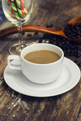 Coffee mug made of ceramic white and coffee beans in a wooden spoon on a wooden floor.