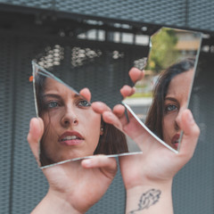 Beautiful girl looking at herself in a broken mirror