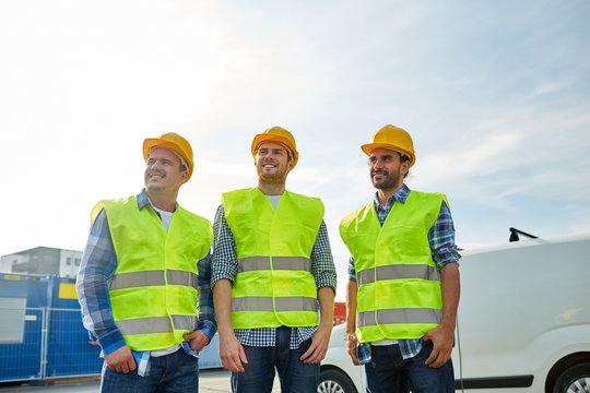 happy male builders in high visible vests outdoors