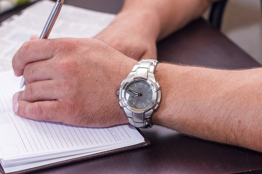 Business hand with the clock, holding pen and notebook