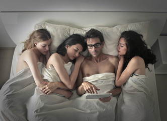 Man using a tablet while sleeping with three women