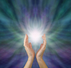 Sensing  Healing Energy - Female healing hands reaching up to white light emerging from radiating green and purple ethereal energy formation background with copy space above. 