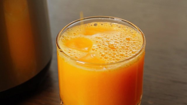 Preparation of orange juice. Drops fall into a glass of juice.