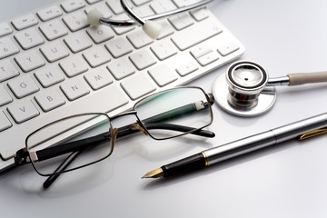 Stethoscope on a table with keyboard and glasses