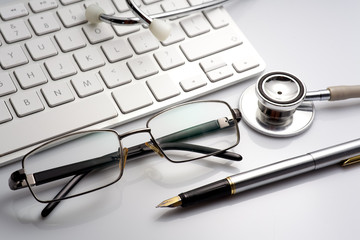 Stethoscope on a table with keyboard and glasses