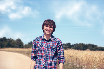 Naklejka na ściany i meble Portrait of happy handsome man with beautiful white smile on blue nature background. Happy young man. Man in the wheat field. 