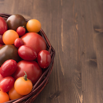 Multi-colored tomatoes at left side of wooden background