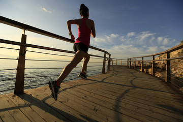 young fitness woman legs running on seaside wooden boardwalk