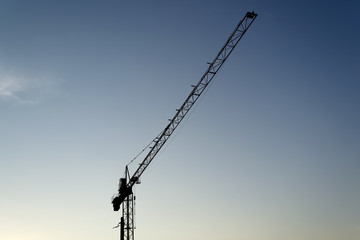 Obraz premium Single building crane silhouette against blue sky in evening