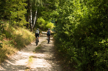 couple cycling with helmets in the hot summer on the green forest trai